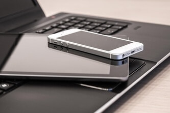 An image of a phone lying on a tablet which is lying on a laptop placed on a table